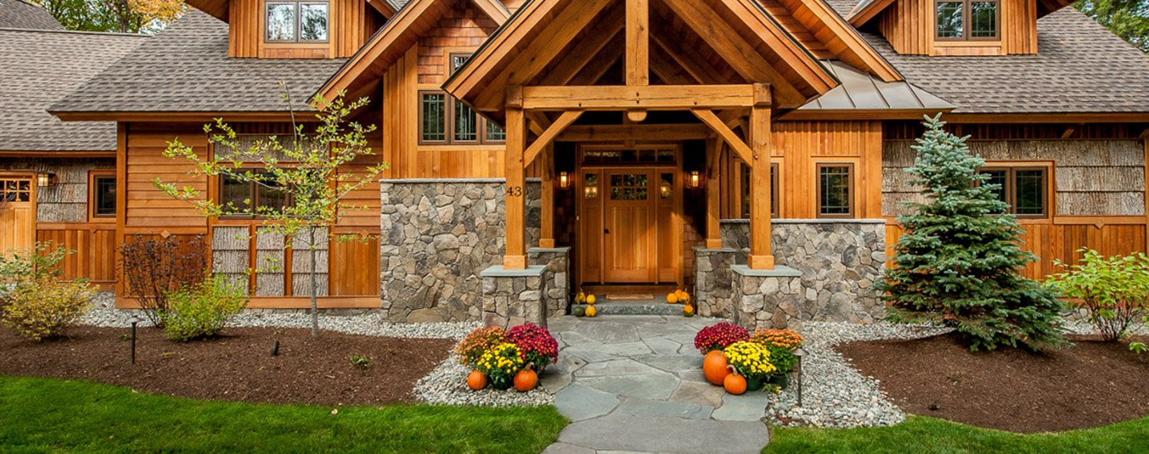 Timber-frame porch on a stone-and-wood house, flagstone walk, mums and pumpkins